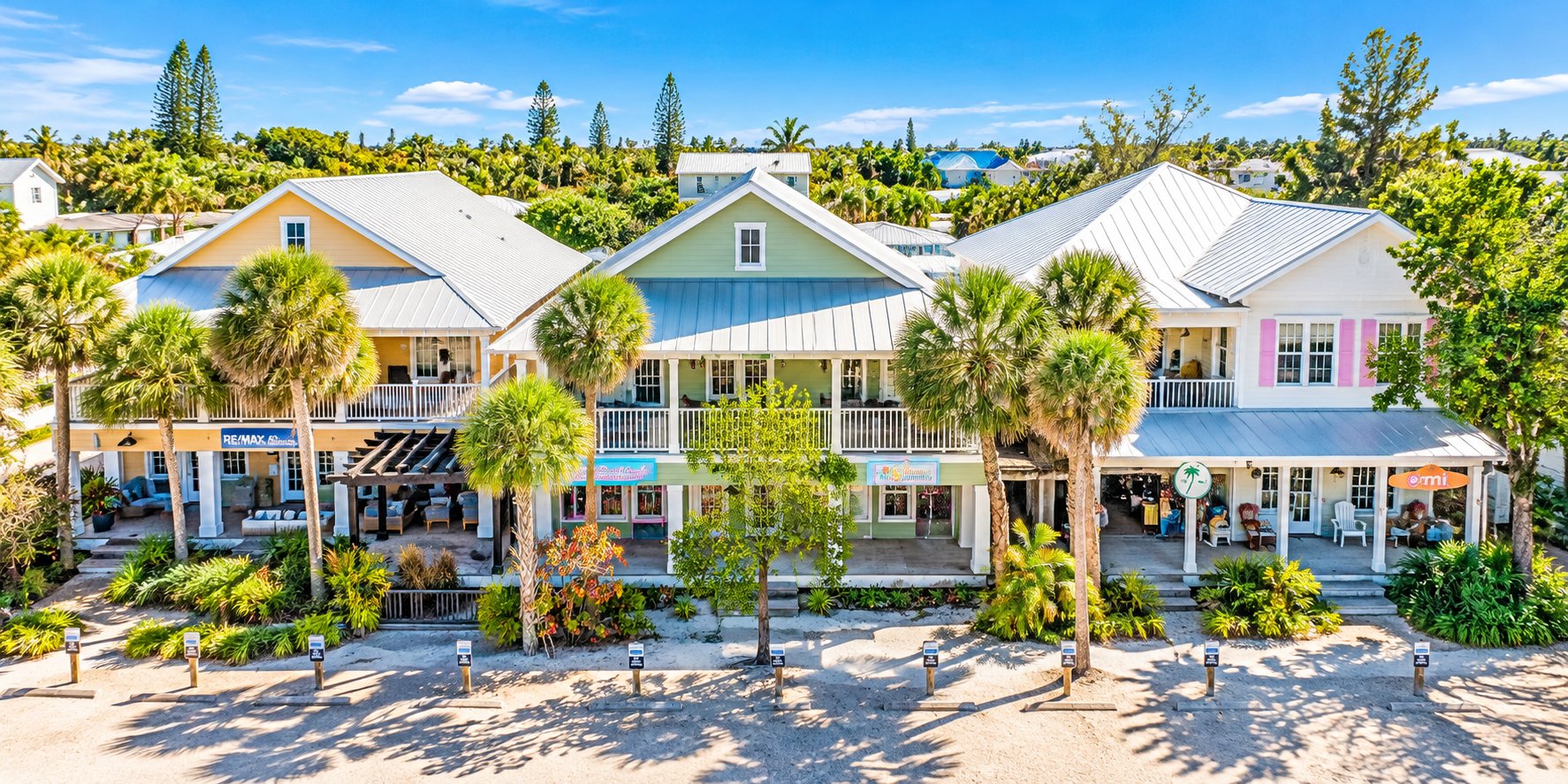 Aerial view of colorful coastal storefronts, palm trees, and vacation accommodations along Pine Avenue on Anna Maria Island, Florida.